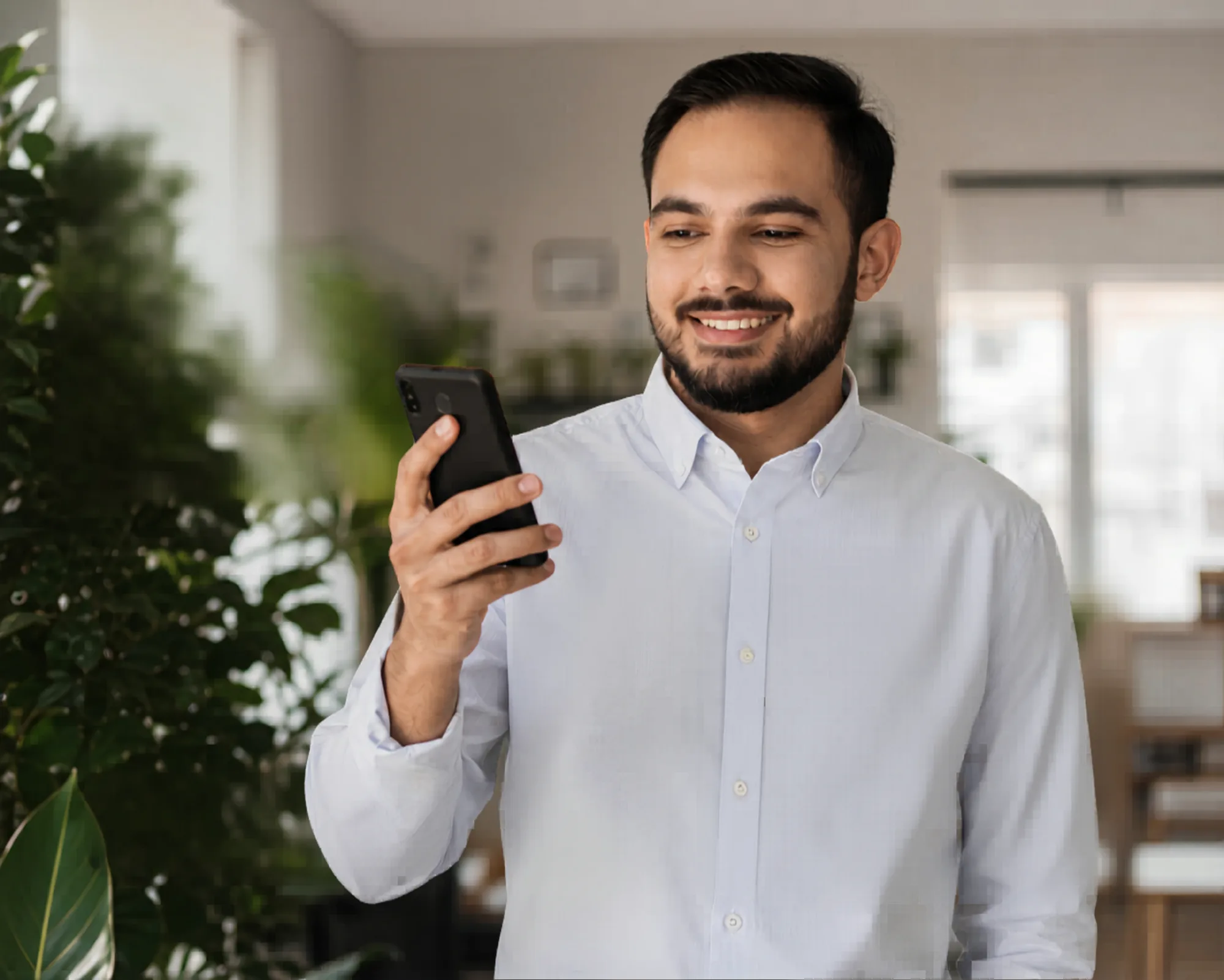 Lächelnder Kunde betrachtet eine moderne Webseite auf dem Smartphone in hellem Büro mit Pflanzen — novum partners: Webdesign und datenschutzfreundliches Tracking